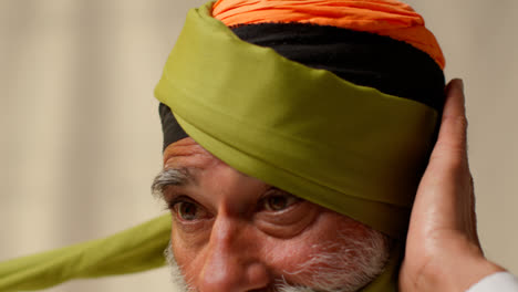 Nahaufnahme-Eines-älteren-Sikh-Mannes-Mit-Bart,-Der-Stoff-Für-Einen-Turban-Vor-Einfachem-Hintergrund-Bindet-1